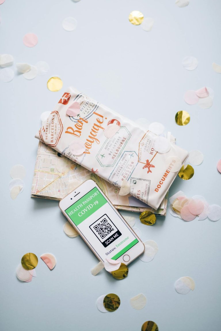 Flat lay of travel essentials featuring COVID-19 health passport displayed on a smartphone.